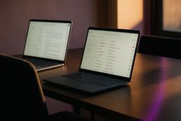 Deux ordinateurs portables affichant des boîtes mail remplies d’auto‑réponses, avec une chaise vide au premier plan, suggérant l’absence d’un lecteur humain.